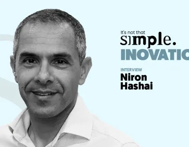 A black-and-white close-up portrait of Niron Hashai, with a light blue background and the text “It’s not that simple. An interview on innovation.”