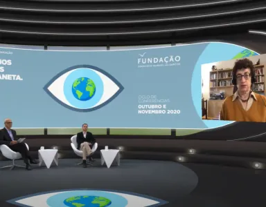 Entrevista virtual, com dois homens sentados em cadeiras num estúdio, e a historiadora de Ciência Naomi Oreskes a falar, numa tela, com o texto "DE OLHOS POSTOS NO PLANETA" e o logotipo da Fundação.
