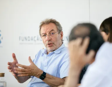 Homem a falar e a gesticular, fundo branco com o logótipo da Fundação.