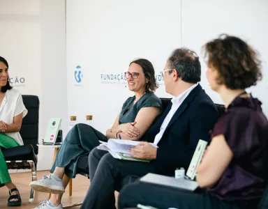 Quatro pessoas sentadas em cadeiras, a debater, com o logo da Fundação ao fundo.