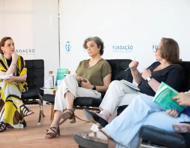 Três mulheres sentadas em cadeiras, num debate da Fundação. Livro visível à frente.