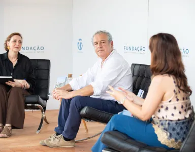 Três pessoas, sentadas em cadeiras pretas, a debater num evento da Fundação. Logotipo "Fundação" ao fundo.