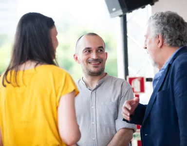 Três pessoas à conversa, a sorrir e a interagir num ambiente ensolarado.