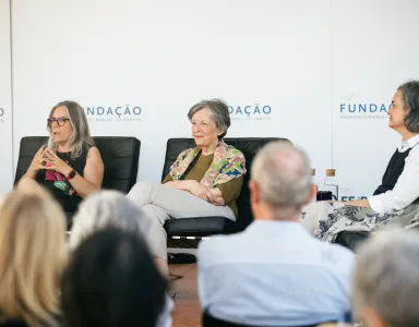 Painel composto por três oradoras sentadas em cadeiras pretas, com público a assistir. Texto ao fundo: "Fundação".