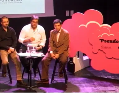 Três homens sentados em cadeiras durante um evento sobre "Pseudociência".