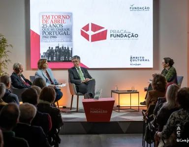 Quatro pessoas sentadas num palco. Atrás, um ecrã com a capa de um livro da Fundação e com o texto "Praça da Fundação".