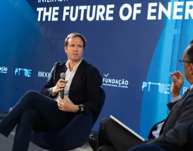O jornalista britânico Ed Conway em palco, sentado, com um microfone na mão. O entrevistador de costas. Fundo azul com o texto "The Future of Energy". DR/FFMS