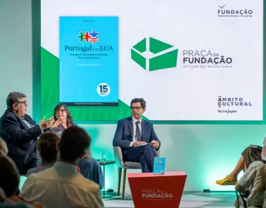 Imagem de quatro pessoas a conversar perante uma plateia,  sob um fundo verde.