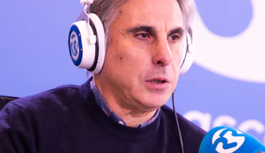 Retrato do professor João Canário, de fones na cabeça, a falar para um microfone.