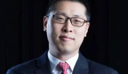 Um homem de fato, com uma gravata vermelha, e de óculos, sob um fundo preto.