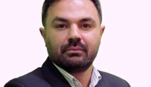 Imagem a cores de um homem, o investigador Arash Reisinezhad, vestido com um fato. Fundo rosa claro.