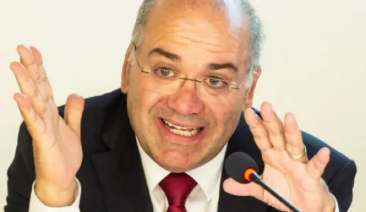 Retrato de um homem, o historiador José Eduardo Franco, a falar para um microfone e a gesticular.