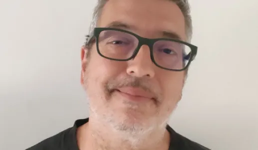 Retrato de um homem de óculos e camisola preta. Fundo claro.