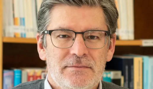 Imagem a cores de um homem, Paulo Miguel Rodrigues, com uma estante de livros a servir de fundo.