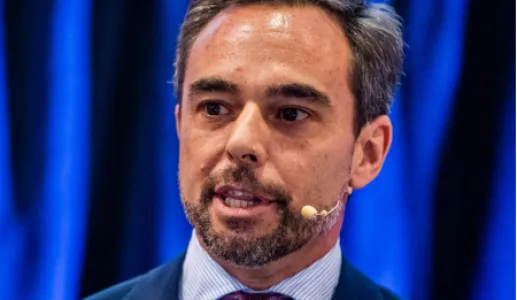 Retrato de um homem de fato com uma gravata roxa, a falar ao microfone.