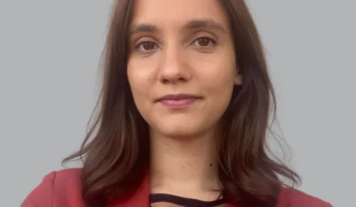 Retrato a cores de uma rapariga, de cabelo castanho e liso, vestido com um casaco vermelho e uma camisola às riscas. 