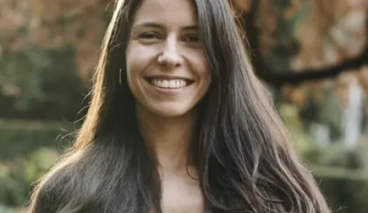 Retrato a cores de uma mulher sorridente. Tem cablo comprido e uma camisa branca.