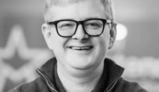 Retrato a preto e branco de um homem sorridente, que usa óculos. Créditos: Eoin Drea