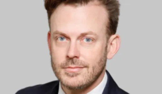 Retrato a cores de um homem de olhos azuis e cabelo castanho. Veste um fato azul. Fundo cinzento claro. Créditos:CNAS