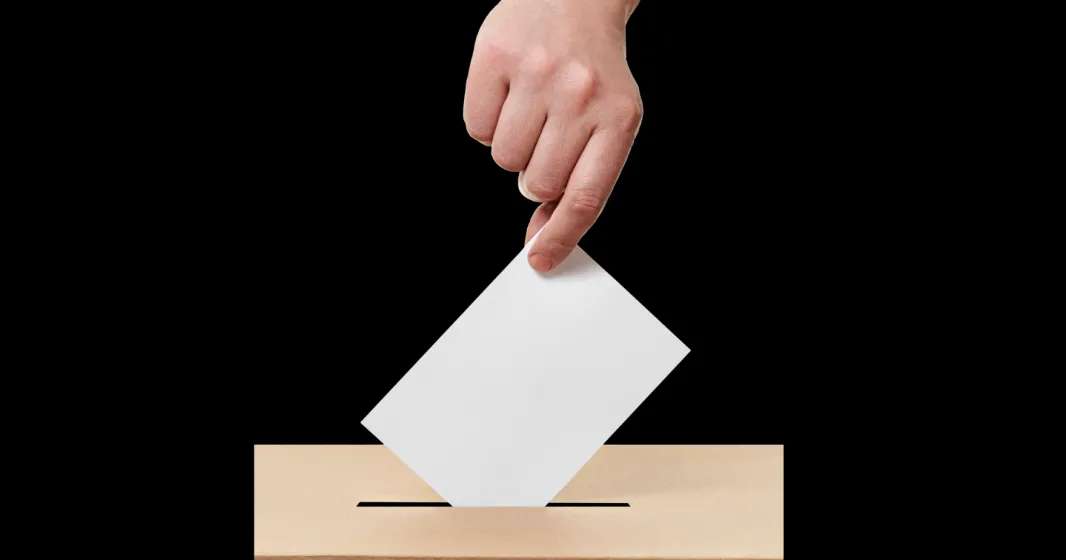 Imagem de uma mão a colocar o voto na urna eleitoral. Crédito: Canva