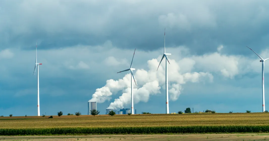  Turbinas eólicas e tubos industriais com fumo a sair num dia nublado na Alemanha. Créditos shutterstock