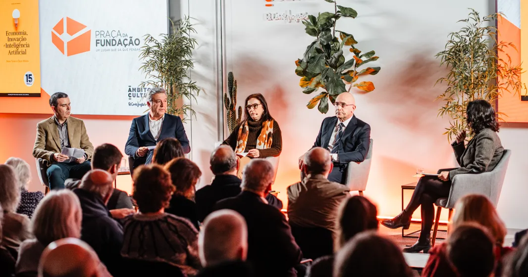 Uma plateia sentada, de costas, a olhar para um palco onde estão quatro oradores, entre eles Pedro Passos Coelho e Elvira Fortunato.