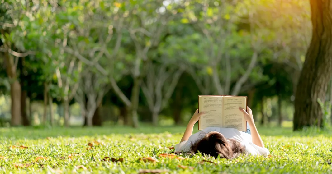 Uma rapariga jovem está a ler deitada na relva de um parque. Crédito: Shutterstock