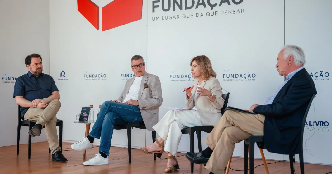 Quatro pessoas sentadas em cadeiras pretas, a debater entre si. Ao fundo, o texto "Praça da Fundação"