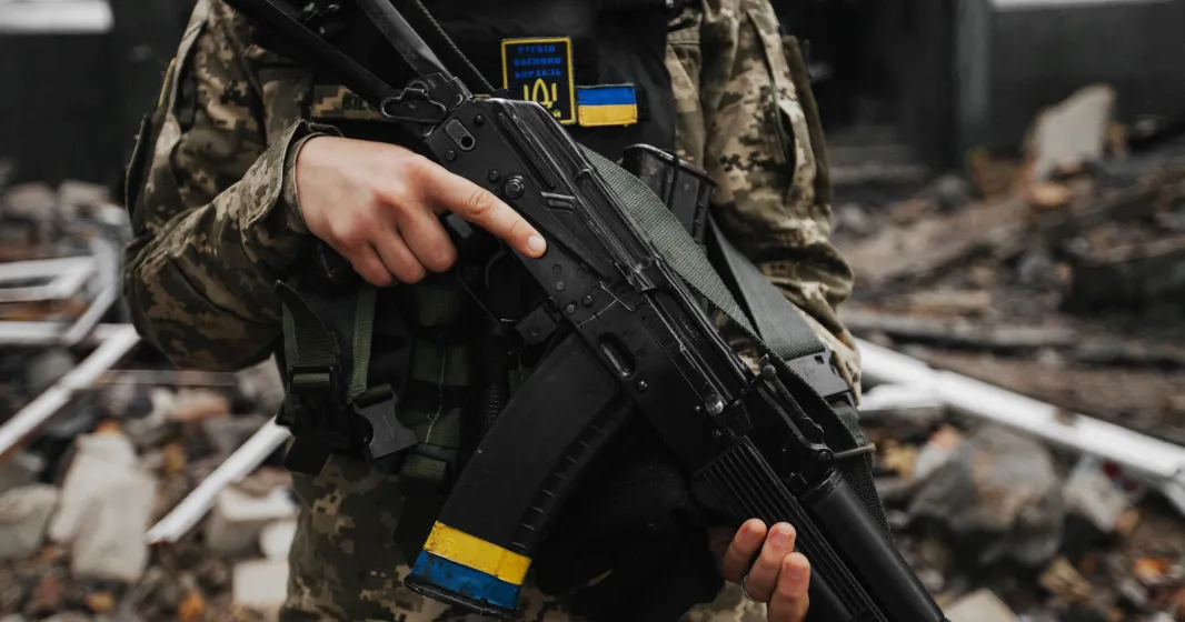 Um soldado carrega uma arma ao peito, com a bandeira ucraniana destacada no seu colete de proteção. Créditos: shutterstock