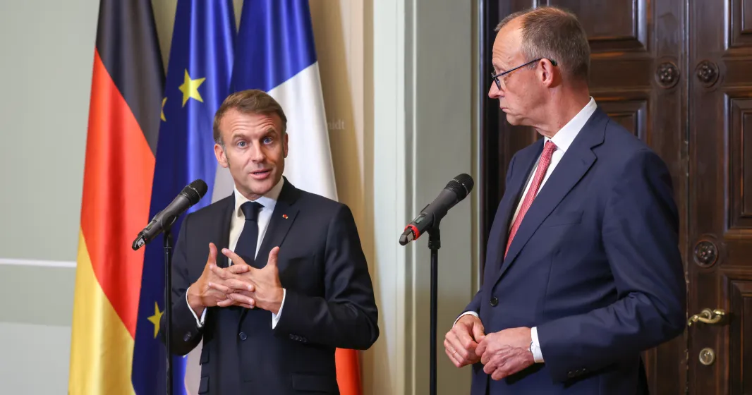 Emmanuel Macron e Friedrich Merz, lado a lado, durante uma conferência de imprensa conjunta. Bandeira de França, Alemanha e da UE ao Fundo. Créditos: shutterstock