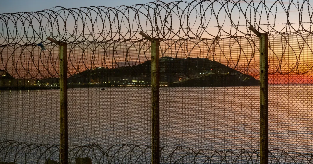 Ceuta, cidade espanhola no norte da África, vista do Marrocos atrás de uma cerca de arame espinhoso localizada na fronteira marroquina, contra um deslumbrante pôr do sol sobre o mar. Crédito: Shutterstock