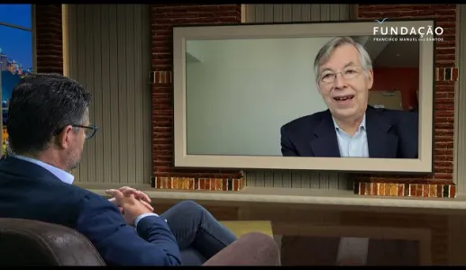 O jornalista Pedro Pinto, num estúdio de televisão, a olhar para uma tela que mostra François Heisbourg a falar.