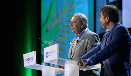 Dois homens num palco, um deles, Jaime Gama, atrás de um púlpito com o texto "FUNDAÇÃO" visível. Fundo verde.