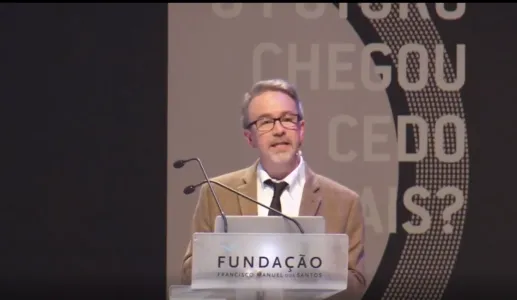 Homem a fazer uma apresentação em palco, num púlpito que tem o logo da Fundação.