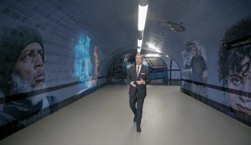 O jornalista Carlos Daniel a andar num túnel com murais de rostos e texto nas paredes.