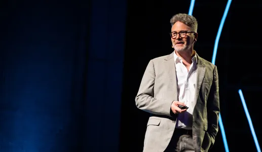 O historiador Adam Tooze a falar numa conferência, com um comando na mão, sobre um fundo escuro-