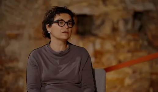 A economista Susana Peralta a falar, sentada numa cadeira. Parede de pedra ao fundo.