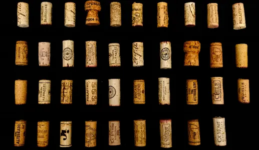 Várias cortiças de garrafas de vinho, dispostas em grelha, sobre fundo preto.
