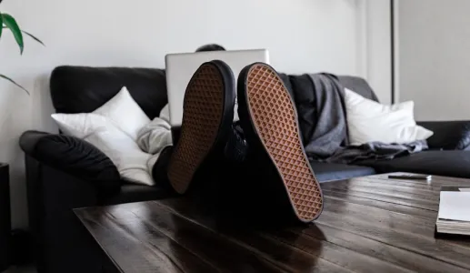 Pés pousados em cima de uma mesa de uma pessoa que está recostada no sofá.
