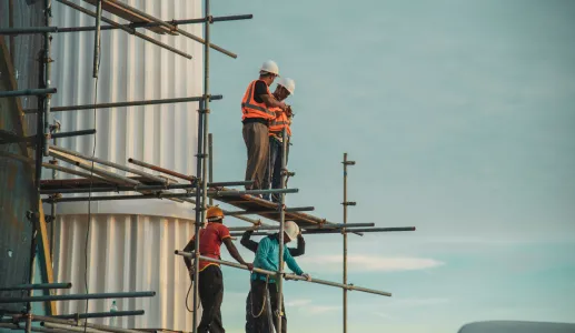 Imagem de trabalhadores da construção civil num andaime de um prédio em construção.