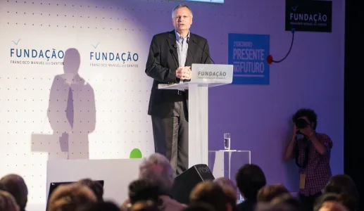 O professor Dani Rodrick a discursar, num púlpito, para uma plateia. Fundo com o logo da Fundação.