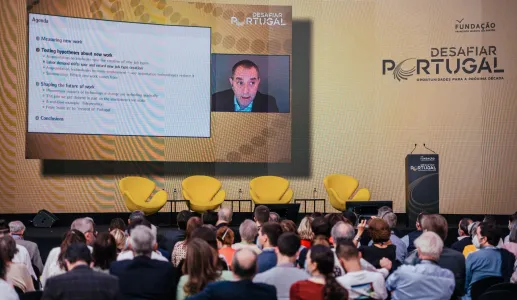 Plateia a olhar para uma tela na qual se vê David Autor a falar. Texto: "Desafiar Portugal". 