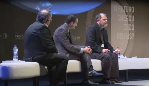 O economista Tyler Cowen a discursar, sentado num sofá branco, ao lado de dois homens. Fundo cinzento, com o logotipo da Fundação e com o texto: "O futuro chegou cedo demais?".