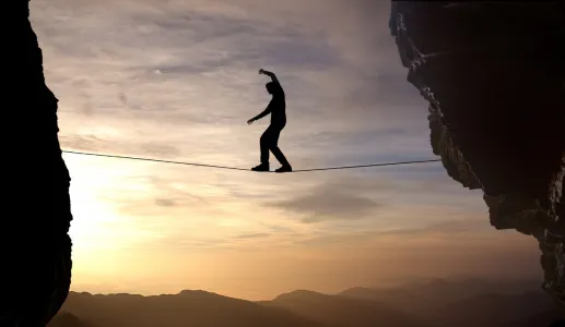 Imagem de um homem a caminhar numa arame suspenso entre duas rochas. Crédito: Canva