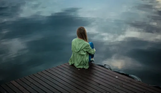 Imagem de uma mulher de costas, pensativa, junto a um lago. Crédito: Keenan Constance/Canva