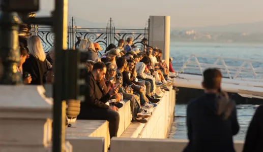 Pessoas de várias idades estão sentadas junto ao rio tejo, em Lisboa, ao entardecer. Crédito: Shutterstock