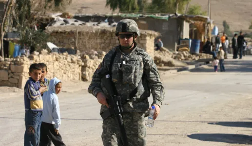 em grande plano um soldado norte-americano junto a uma estrada no Iraque, enquanto ao fundo várias crianças apontam para o militar. Crédito: Shutterstock