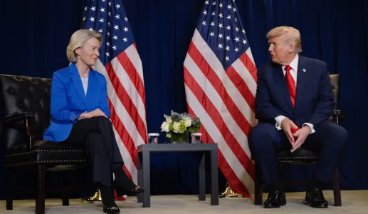 Ursula von der Leyen sentada ao lado de Donald Trump, com duas bandeiras dos EUA atrás.