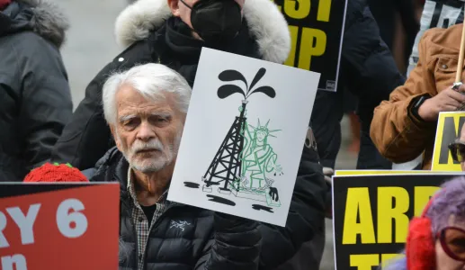 Uma manifestante em NY a segurar um cartaz com uma ilustração da estátua da liberdade a agarrar uma torre de petróleo. Créditos: shutterstock