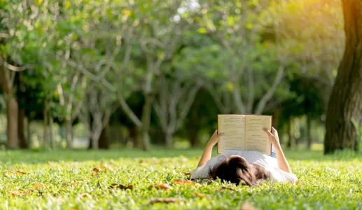 Uma rapariga jovem está a ler deitada na relva de um parque. Crédito: Shutterstock